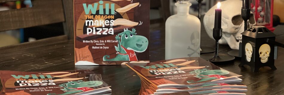 30 copies of Will The Dragon Makes Pizza to be donated to local libraries sits on a wooden table with halloween decorations.